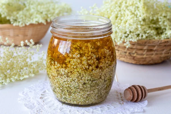 A jar filled with fresh elder flowers and honey, to prepare homemade herbal syrup