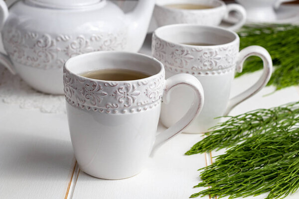 Two cups of horsetail tea with fresh Equisetum arvense plant on a white wooden table
