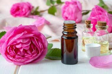 A dark bottle of essential oil with roses on a white table clipart