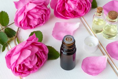 A bottle of essential oil with fresh roses on a white table clipart