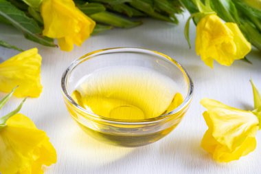 Evening primrose oil in a bowl with fresh blooming plant  clipart
