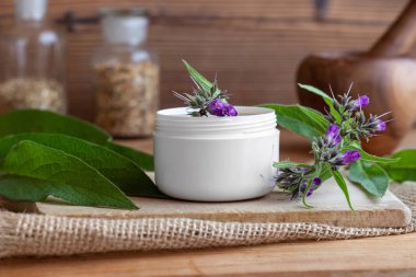A jar of comfrey root ointment with fresh blooming symphytum officinale plant clipart