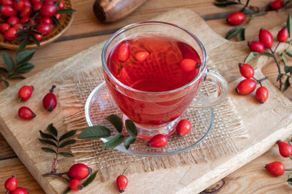 A cup of rose hip tea with fresh plant on a table
