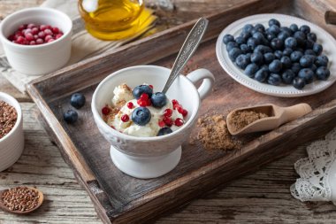 Toprak keten tohumlu süzme peynir, yabanmersini ve donmuş kızılcık, fonda kırmızı frenk üzümü ve keten tohumu yağı.