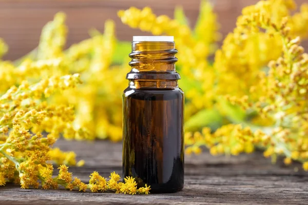Egy üveg aranyvessző illóolaj és virágok — Stock Fotó