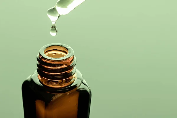 A bottle of essential oil with a dropper on a green background