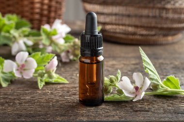 İçinde taze Althaea resmi çiçekleri olan koyu renkli bir marshmallow kökü tentürü.