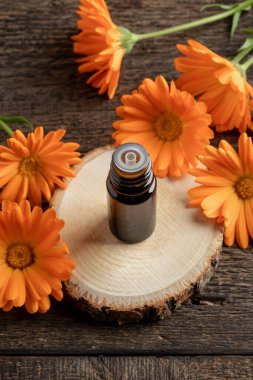 Ahşap bir masanın üzerinde taze takvim çiçekleri olan bir şişe gerekli yağ.