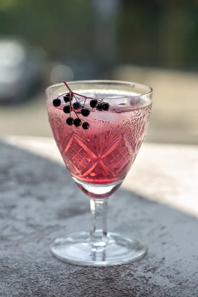 Water with ice and black elder syrup, decorated with elderberries, outdoors