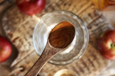 Elma sirkesi ahşap bir kaşıkta, bir bardak suyun üstünde, üst manzara.