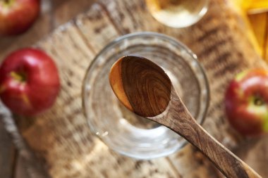 Elma sirkesi ahşap bir kaşıkta, bir bardak suyun üstünde, üst manzara.