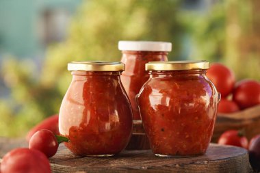 Three jars of homemade tomato and sweet pepper relish (ajvar-style vegetable spread, chutney or bruschetta topping) on a table outdoors