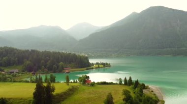 Turkuaz alp gölü, çayır evleri, ormanlar ve tepeler.
