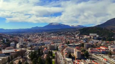 Gökyüzünde bulutlar olan güneşli bir günde evleri, yolları ve dağ manzaralarını gösteren Fransa Gap şehrinin manzarası