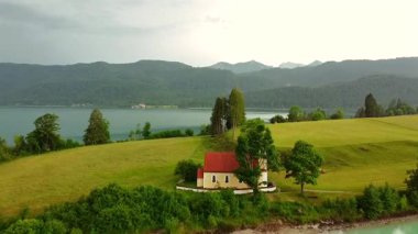 Küçük şapel yamaçlı göl ve dağların havadan yakından görüntüsü.