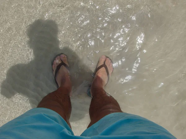 Bacaklar ile mavi şort ve flip flop, Tayland denizin temiz su ayakta giyen adamın.