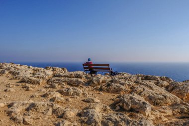 Bir genç landy sessizce için Cape Greco Kıbrıs'ta denize bakan bir bankta oturan arkadan görünüş.