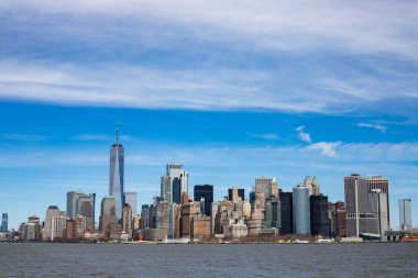 Aşağı Manhattan 'ın ikonik silueti New York' ta, etrafındaki binaların hemen üstünde duran bir Dünya Ticaret Merkezi ile birlikte. Suyun üzerinde çekilen bu görüntü, şehrin mimari çeşitliliğini ve ihtişamını yansıtıyor..