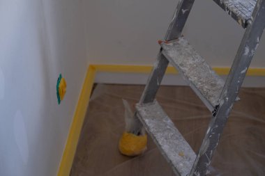 Eski merdiven ve duvar tabanının olduğu bir iç mekan. Daire yenileme sırasında boyama için maske bandıyla hazırlanmış. DIY, ev projeleri, iç tasarım ve emlak yenileme için mükemmel..