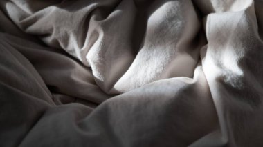 Yumuşak doğal ışık ve gölgeli buruşuk bej kumaş yakın plan, desenli bir arka plan yaratır. Tekstil tasarımı, iç konseptler, ürün modellemeleri ve minimalist yaşam tarzı temaları için ideal.