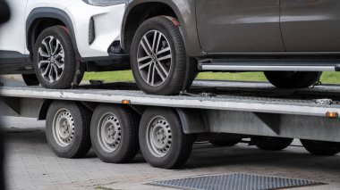 Tekerleklere ve dingillere odaklanmış iki aracın karavan platformuna yakın çekim görüntüsü. Bu resim ulaşım, çekici hizmetleri, araba teslimatı ve otomotiv ile ilgili bağlamlarda kullanmak için uygundur