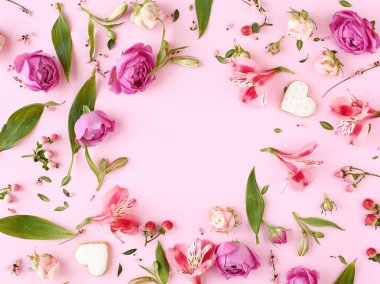 Pembe gül çiçekleri, dallar, yapraklar ve kalp şeklinde kurabiyelerden oluşan bir çerçeve. Düz yerde, üst tarafta. Romantik konsept.