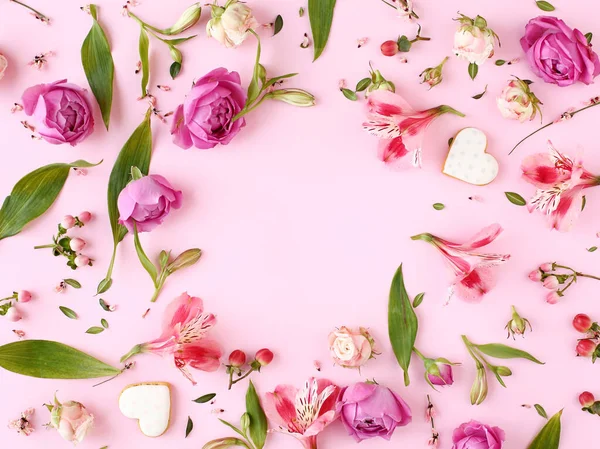 Pembe gül çiçekleri, dallar, yapraklar ve kalp şeklinde kurabiyelerden oluşan bir çerçeve. Düz yerde, üst tarafta. Romantik konsept.