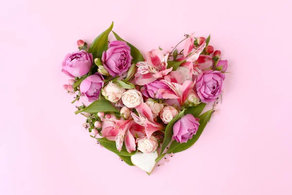 Pembe arka planda gül çiçekleri, dallar, yapraklar ve kurabiyelerden oluşan kalp şeklinde bir çiçek bileşimi. Düz yerde, üst tarafta. Romantik konsept.