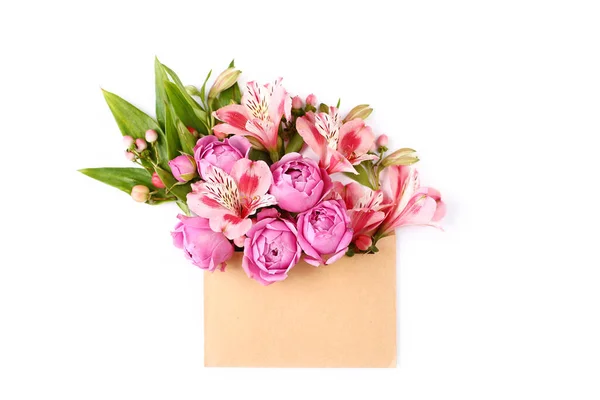 Pink flowers and green leaves in craft envelope. Floral composition flat lay on white background.