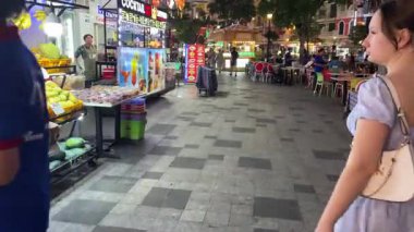 Bir kız turist cadde üzerindeki bir kafede yürüyor insanlar gece aydınlatma gecesi Grand World 'de nehir kenarında oturuyorlar. Vietnam Phu Quoc Adası 09.05.2025