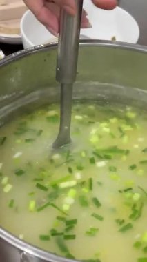 Ot dolu tavuk çorbası, restoranda siyah bir tabakta krema çorbasını süsleyen bir tencere şefinin elinden dökülen bir tabağa dökülüyor. Krema çorbası servis etmek için dekore edildi. Yüksek kalite 4k