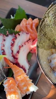 Japon suşi tabağından bir dilim ton balıklı sashimi. Stüdyo ışıkları altında siyah bir arka planda somon, deniz tarağı, yumurta ve garnitürle. Yüksek kalite 4k görüntü