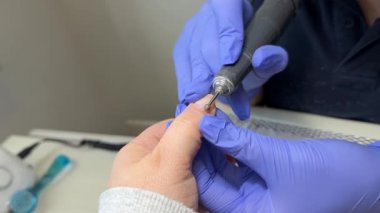 Güzellik salonundaki kadın müşteriler için manikür prosedürü uygulayan usta bir manikürcü. Elektrikli tırnak cilası ile jöle cilası ve fırça kullanarak temiz parmak. Bir manikürcü değirmen makinesiyle çalışır.. 