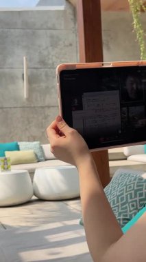 Parktaki çayırda çimlerin üzerinde oturan ve dijital tablet kullanan Kafkasyalı esmer kız. Mutlu kadın tablet ekranına bakıyor Phu Quoc Adası Vietnam 09.11.2025