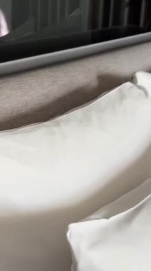 Beyaz bir otel odasında, beyaz bir yatak başlığını aydınlatan beyaz bir lamba ve mükemmel hazırlanmış bir yatağın beyaz keten örtüsü var. Yüksek kalite 4k görüntü