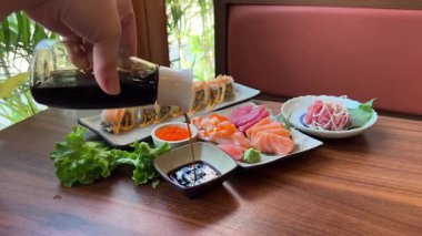 Geleneksel Japon mutfağının en iyi manzarası. Somon, ton balığı ve sebzeli suşi ruloları siyah taş masada servis edilir. Siyah taş üzerinde yemek çubuklarıyla Asya yemeği. Kamera hareketi.