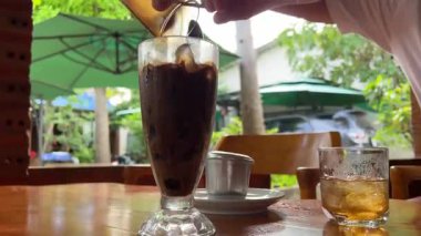 Vietnam kahvesiyle konsantre süt baristasını karıştırıp bir bardak buzlu kahveye karıştırın, yavaş çekimde. Yüksek kalite 4k görüntü