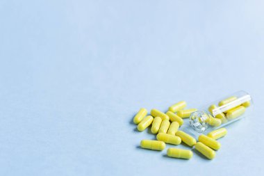 Sarı kapsüller mavi arka plandaki bir şişeden dökülür. Omega-3 vitaminleri. Yiyecek takviyesi. Kapsüllerde balık yağı. Boş alan. Metin için boşluk. kopyalama alanı. Arka plan bulanık. Seçici odak.