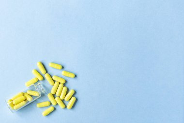 Sarı kapsüller mavi arka plandaki bir şişeden dökülür. Omega-3 vitaminleri. Yiyecek takviyesi. Metin için boşluk. kopyalama alanı. Arka plan bulanık. Seçici odaklanma. Tıp konsepti. Boş alan.