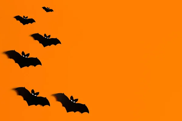 orange background with a flock of black paper bats for Halloween, black paper bat silhouettes on an orange background, Halloween concept, copyspace, flatlay, top view, overhead
