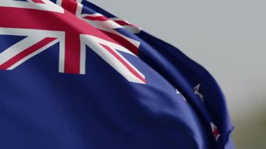 Yeni Zelanda ulusal bayrağının dinamik çekimi parlak bir arkaplan üzerinde hafifçe dalgalanıyor. İngiliz bayrağı ve Güney Haçı 'nın dört canlı kırmızı yıldızı ile birlikte ikonik mavi alanı temsil ediyor.