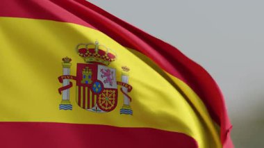 İspanyol bayrağının dinamik tasviri, ikonik kırmızı ve sarı çizgileri ve ulusal arması, rüzgarda gururla sallanıyor.