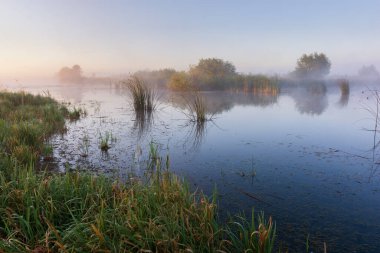 Gölün üzerinde gün doğumu sisli suda yansıyor..