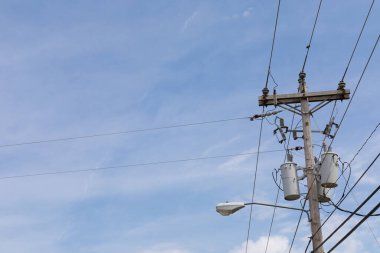 Tahta elektrik direği, fiber optik kablo kabloları, sokak lambası ve transformatörleriyle ince bulutlu mavi gökyüzü, yatay görünümü