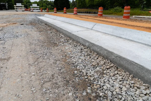 İnşaat halindeki yeni bir caddenin yanında trafik barikatları, beton kaldırımlı çakıl yol yatağı, yatay görünüm.