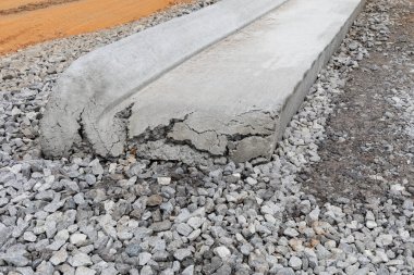 Yuvarlanan beton kaldırımın sonunda inşaat halindeki bir yol yatağı, çakıl tabakası, yatay görünüm.