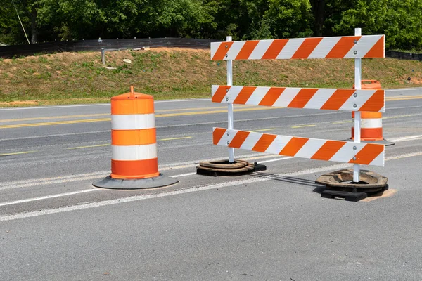 Traffic safety barricade and barrels with orange and white stripes on an asphalt street, horizontal aspect