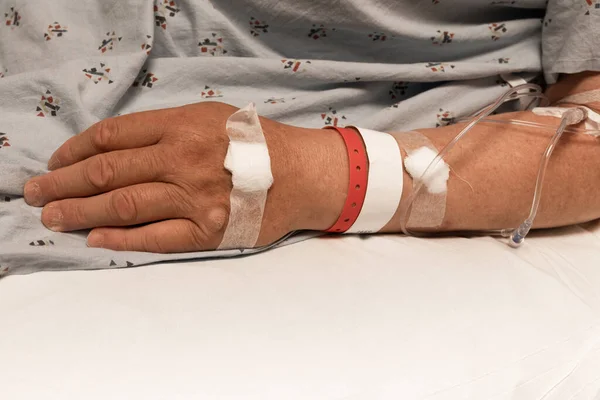 Arm and hand of a man in a hospital gown, IV, wristbands, copy space, horizontal aspect