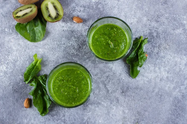 Healthy green smoothie with green apple, spinach, kiwi and almond nuts on gray background