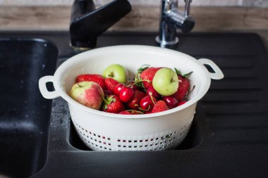 colander with ripe cherries and apples with strawberries in black kitchen-sink , Summer food concept clipart